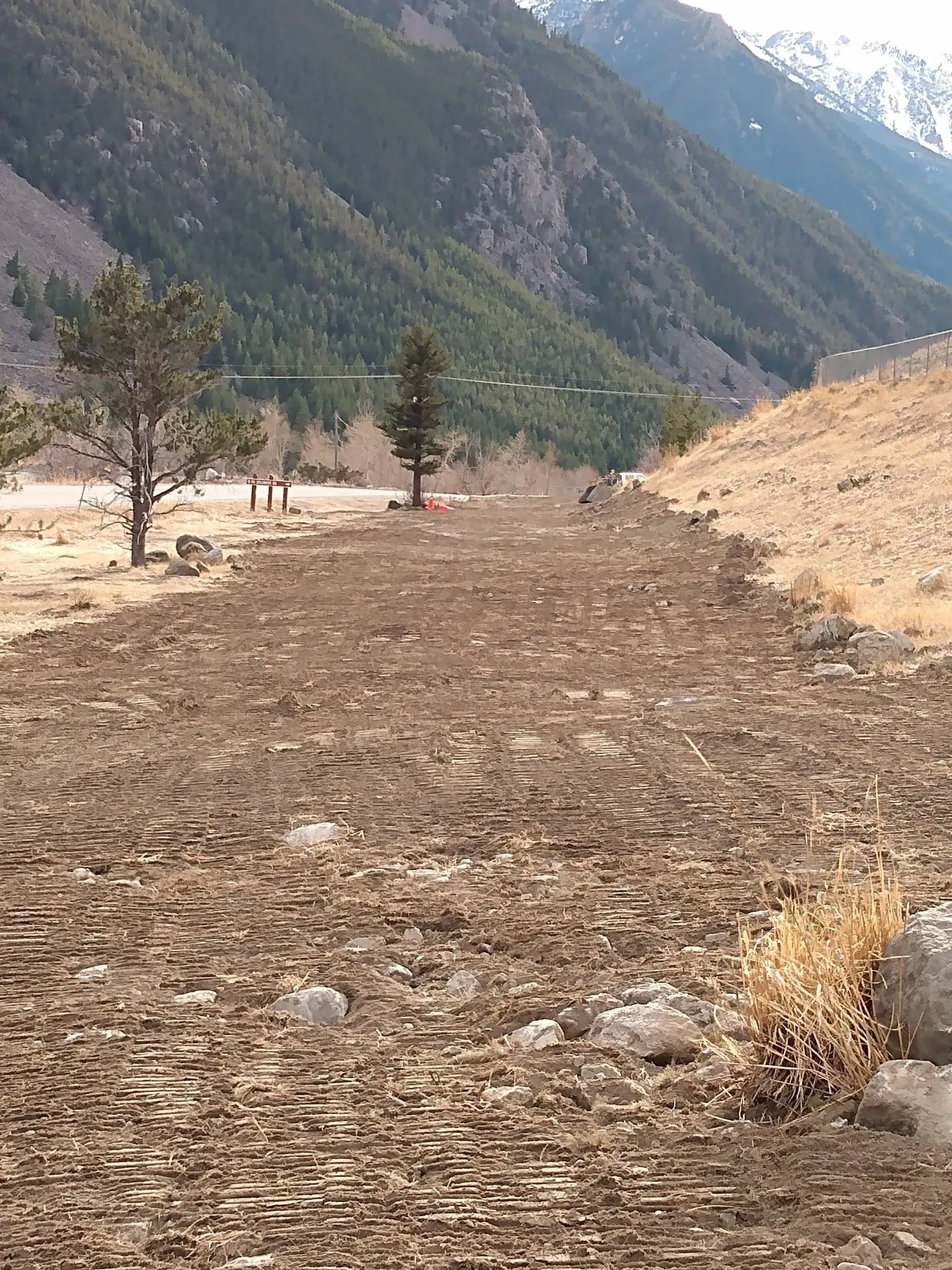 Brown plowed field in a valley, with trees, mountains in the background.