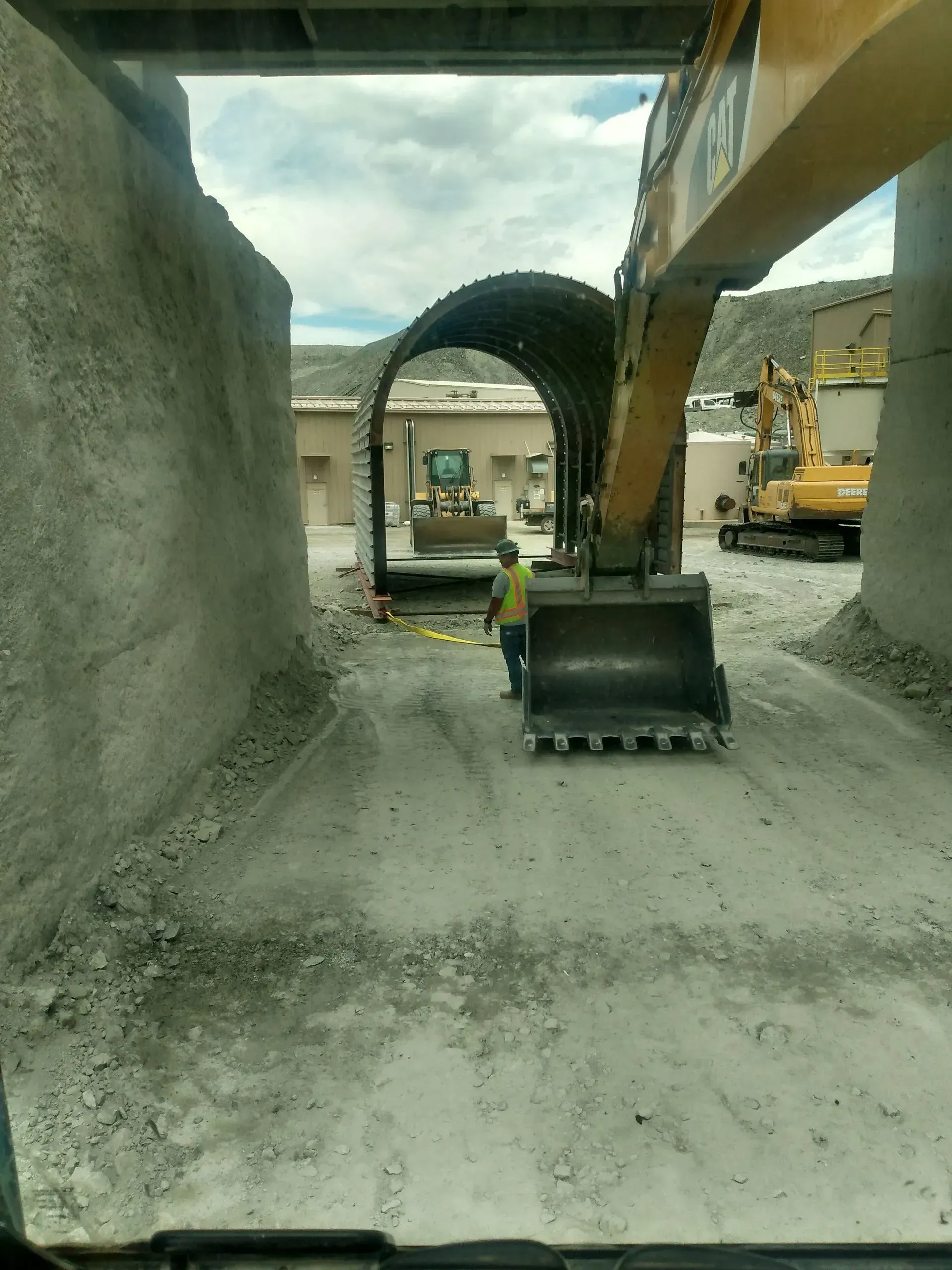 Construction site: Excavator in tunnel, worker, concrete walls and arch, under a bridge.
