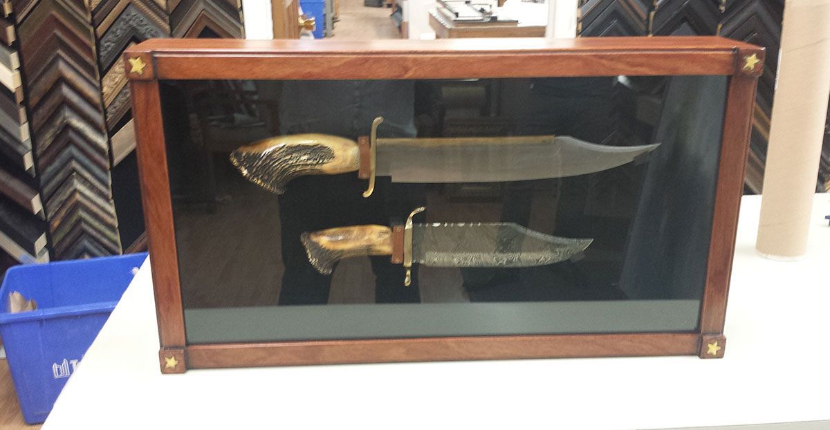 Two knives in a wooden display case with a dark background.