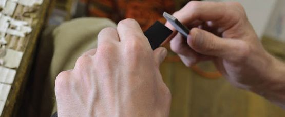Person's hands hold and work with small, dark rectangular pieces, possibly for mosaic art.