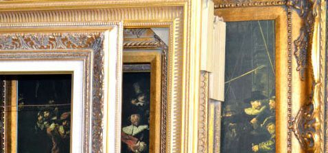 Close-up of ornate gold frames surrounding dark paintings, possibly in a museum or gallery setting.