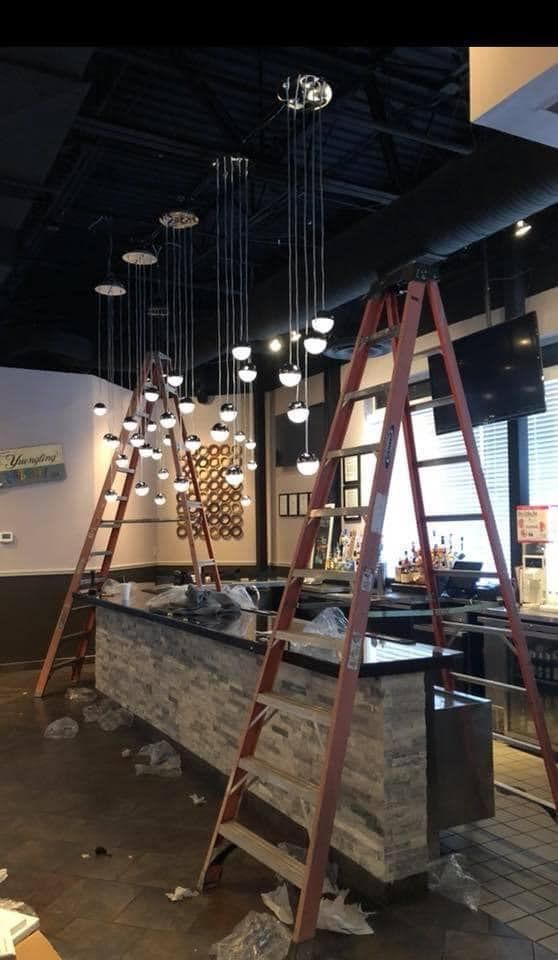 Bar under construction with ladders, hanging globe lights, and a dark countertop.