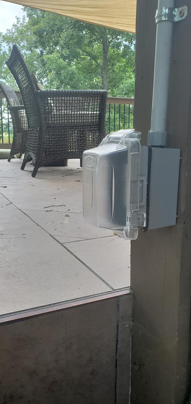 An outdoor electrical box mounted on a brown post next to a patio with wicker furniture.
