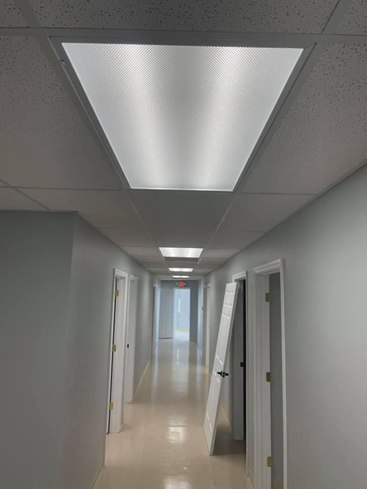 Hallway with fluorescent ceiling lights, pale walls, and doors.