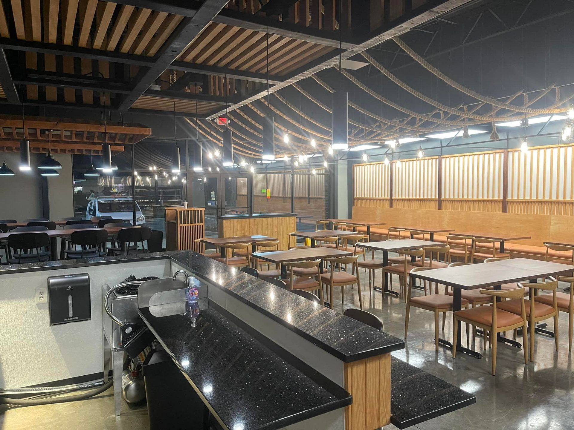 Empty restaurant interior with tables, chairs, and bar, featuring string lights and wooden accents.