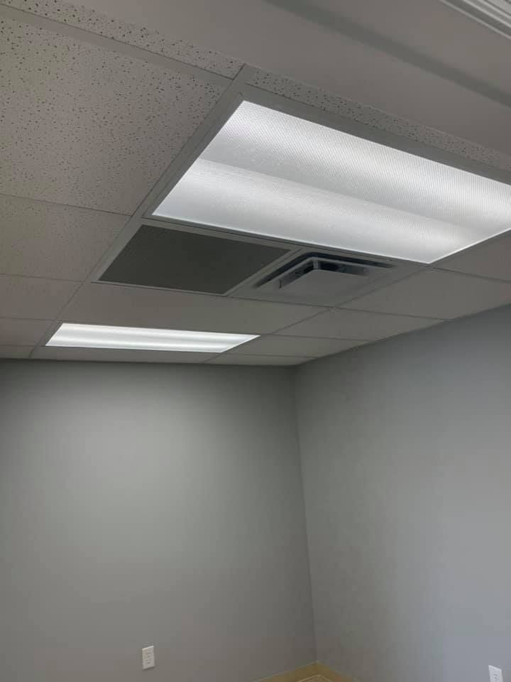 Bright fluorescent ceiling lights in a room with gray walls and a ceiling vent.
