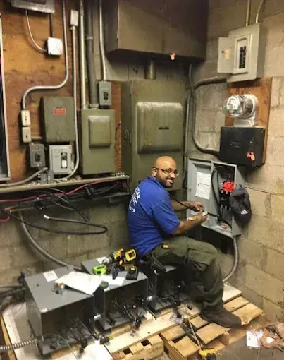 Electrician working on a control panel in an industrial setting. He wears a blue shirt and khaki pants.