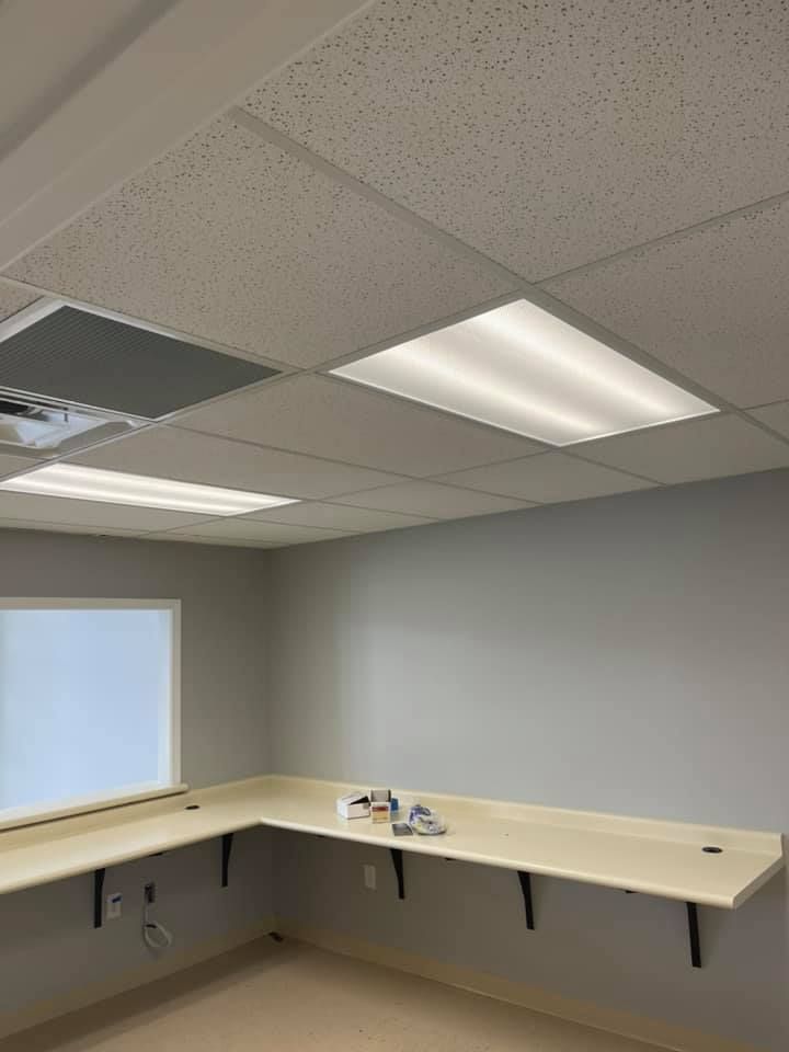 A brightly lit, empty office with a long desk, white window, and gray walls and ceiling.