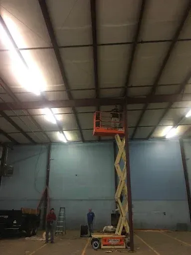 People on scissor lift inside a warehouse. They work on the ceiling.