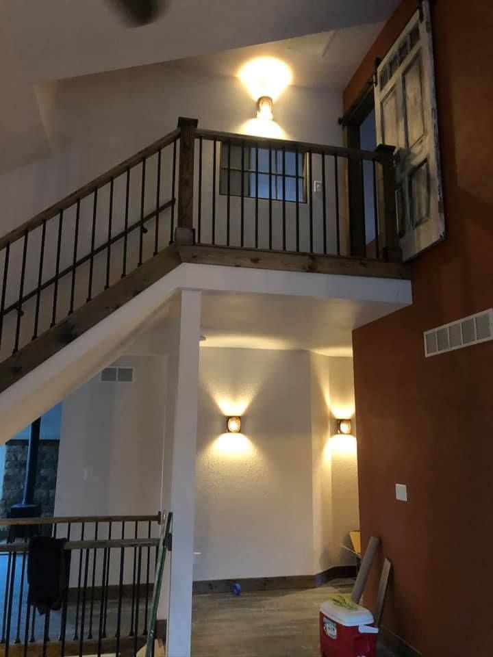 A two-story interior with a staircase, railing, and warm lighting; featuring an open layout with rustic accents.