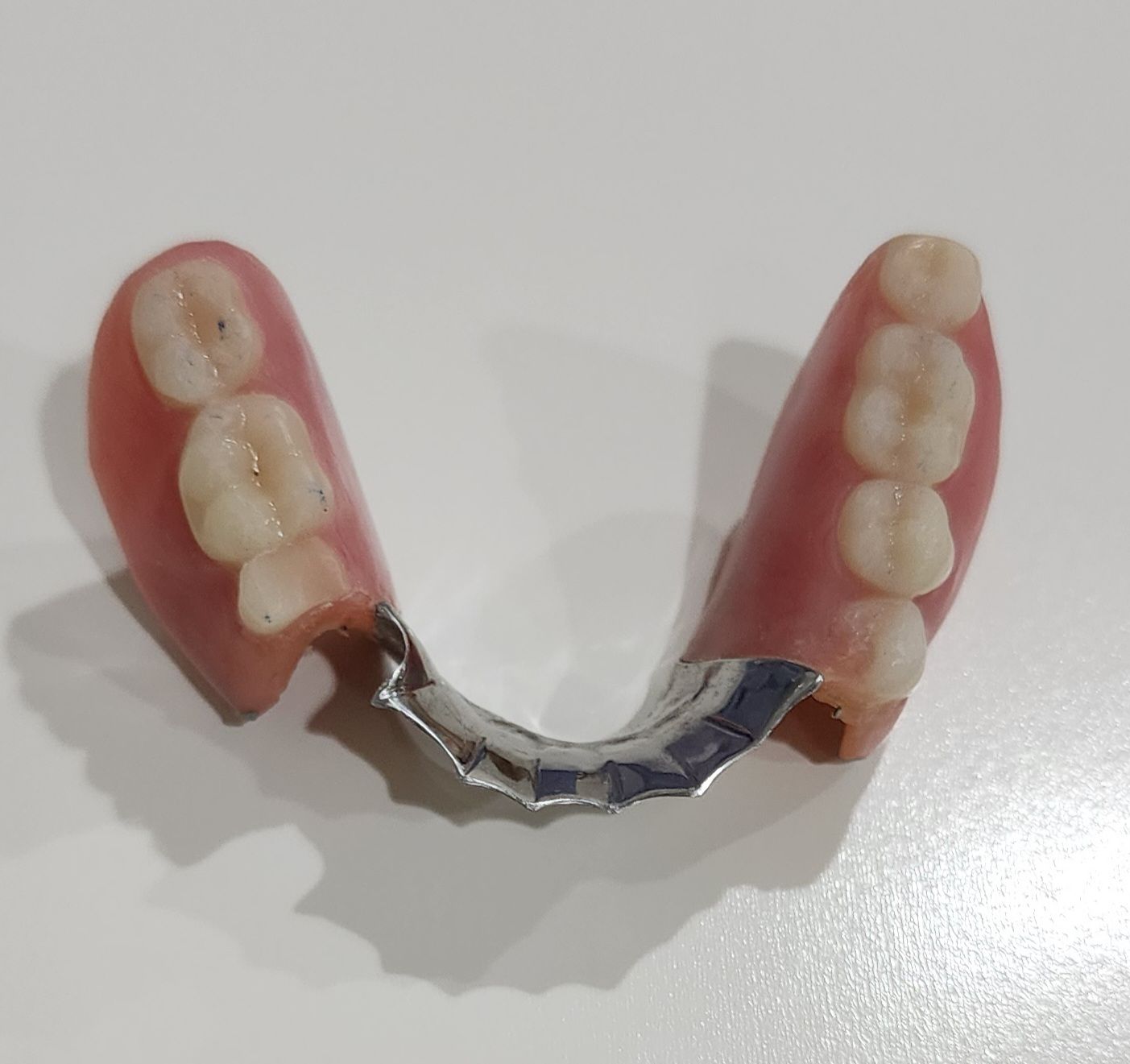 Partial denture with pink gum-colored base and four artificial teeth attached by silver metal clasp.