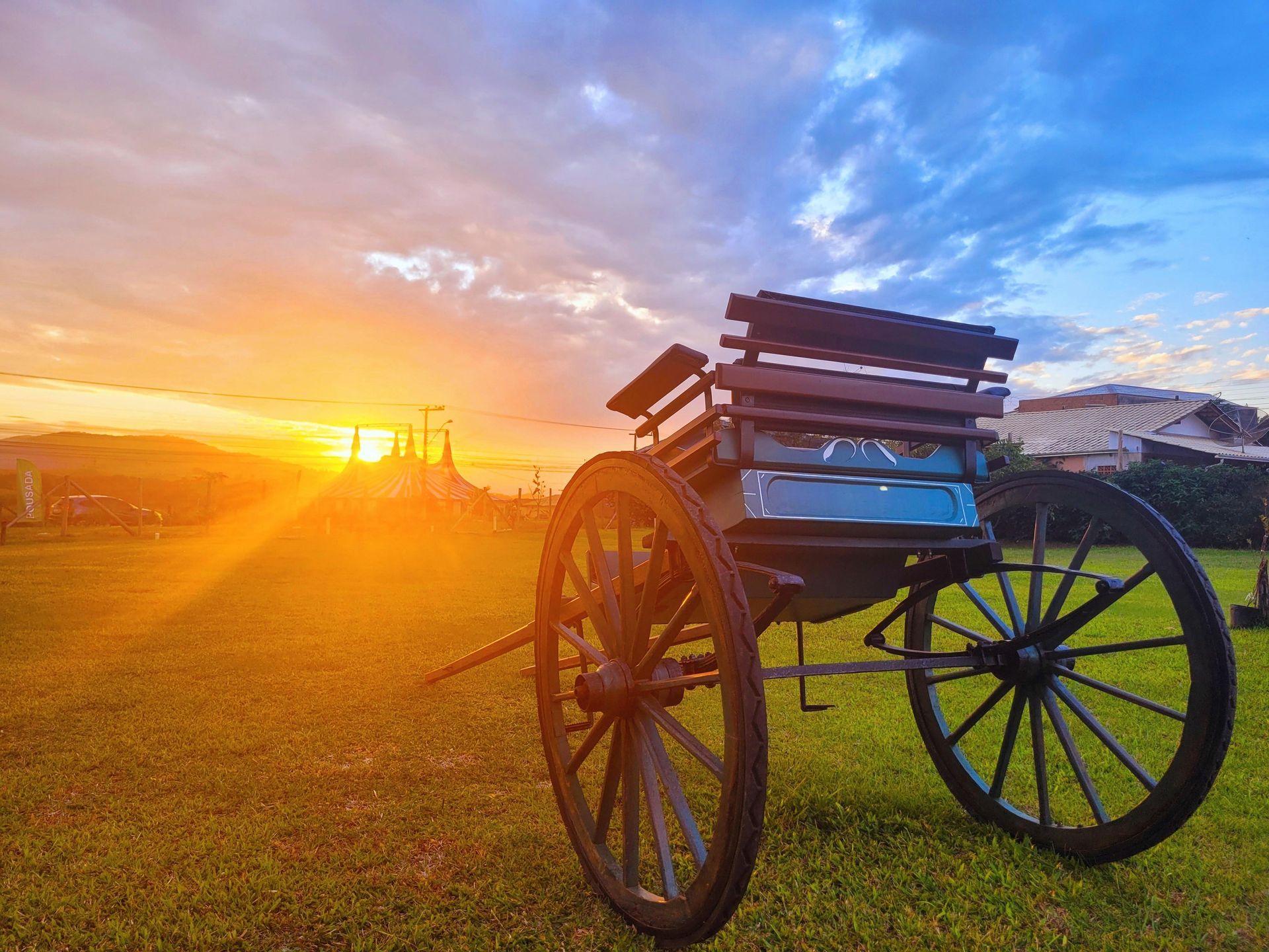 Uma carruagem puxada por cavalos está estacionada em um campo gramado ao pôr do sol.
