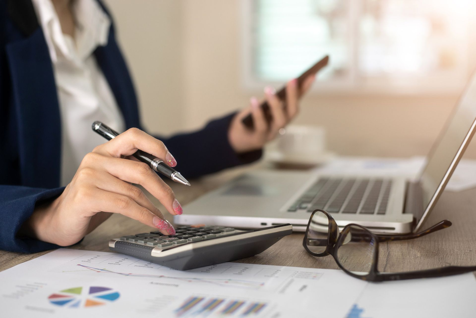 A woman is using a calculator and a laptop while holding a pen. A woman is using a calculator and a laptop while holding a pen.