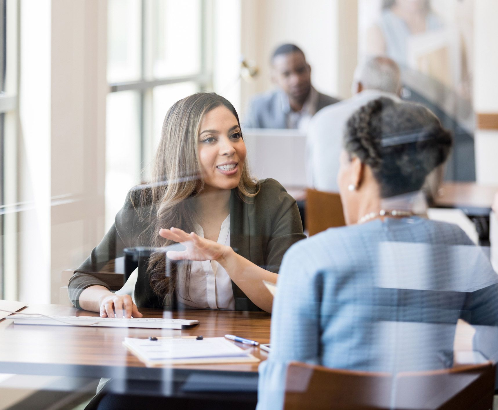 A woman is sitting at a table talking to another woman. A woman is sitting at a table talking to another woman.