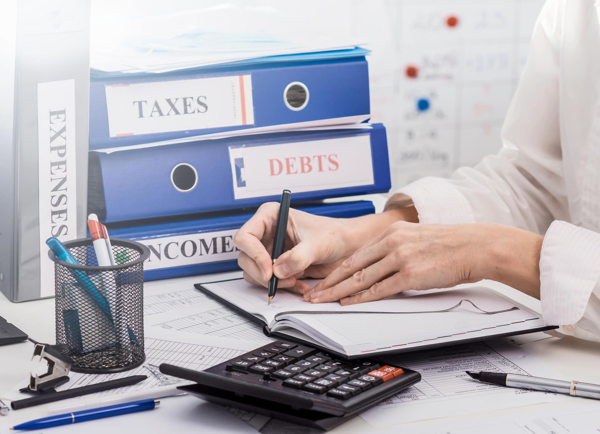 A woman is sitting at a desk using a calculator and writing in a notebook.