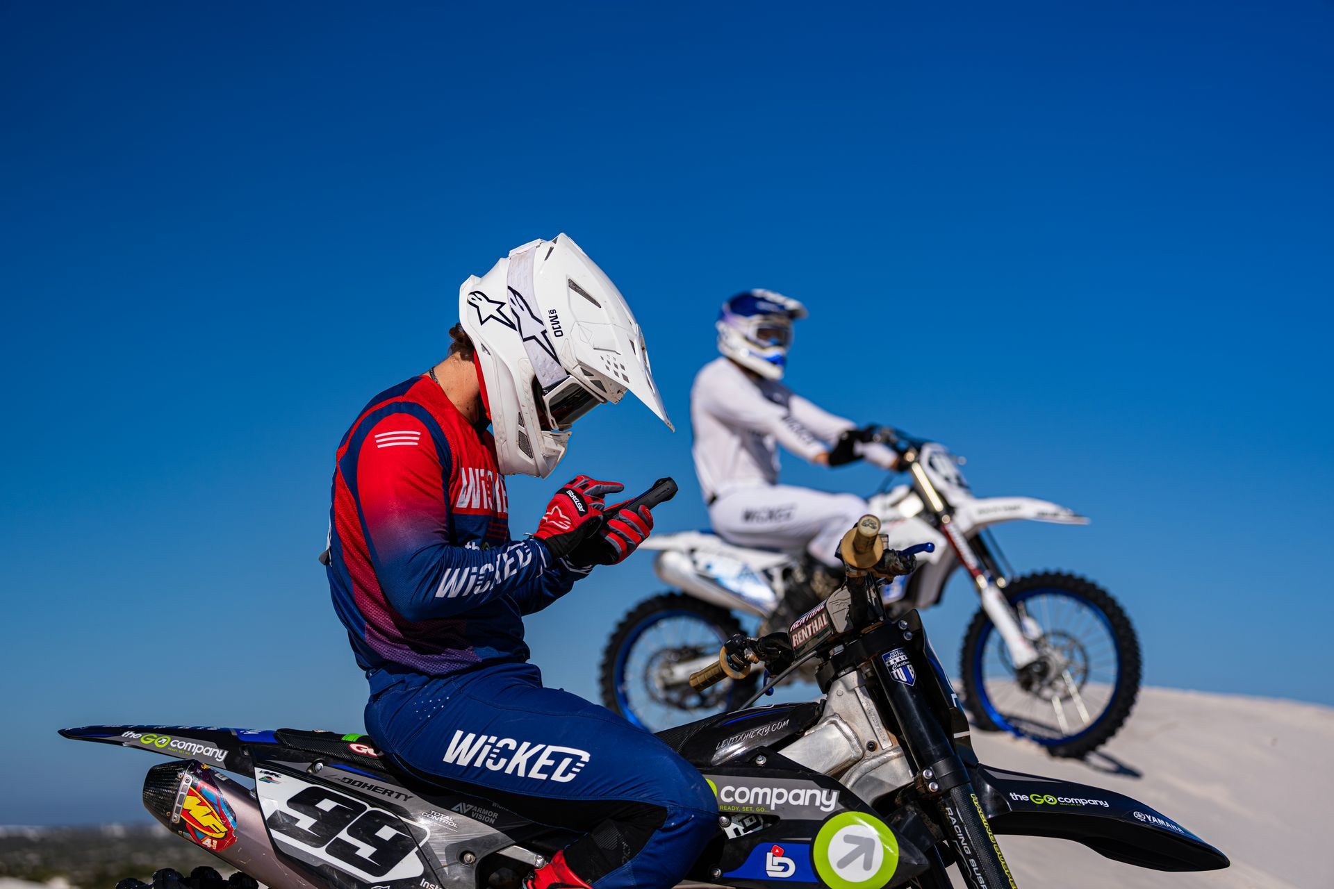 A man is sitting on a dirt bike while another man is riding a dirt bike.