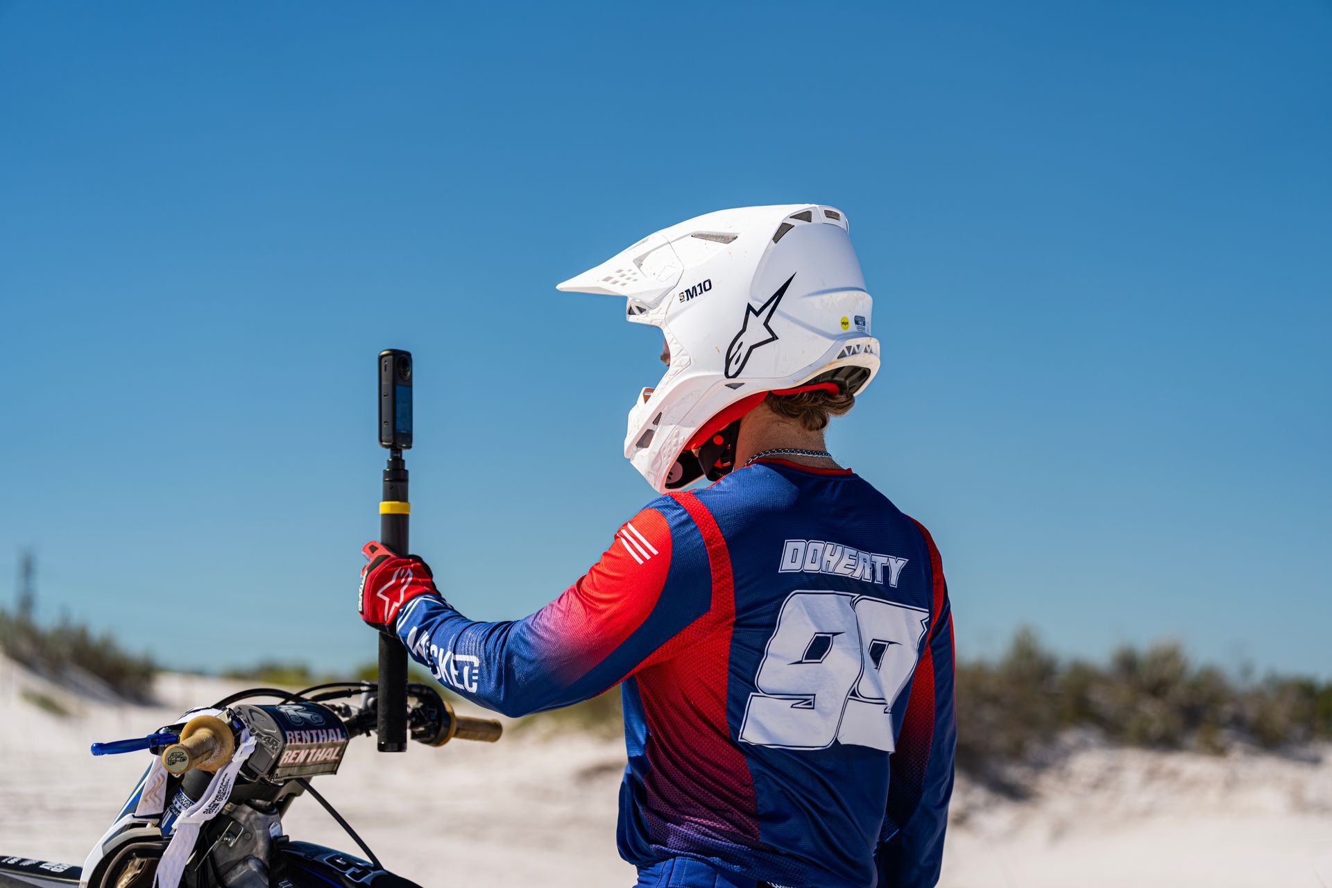 A man is standing next to a dirt bike holding a camera.