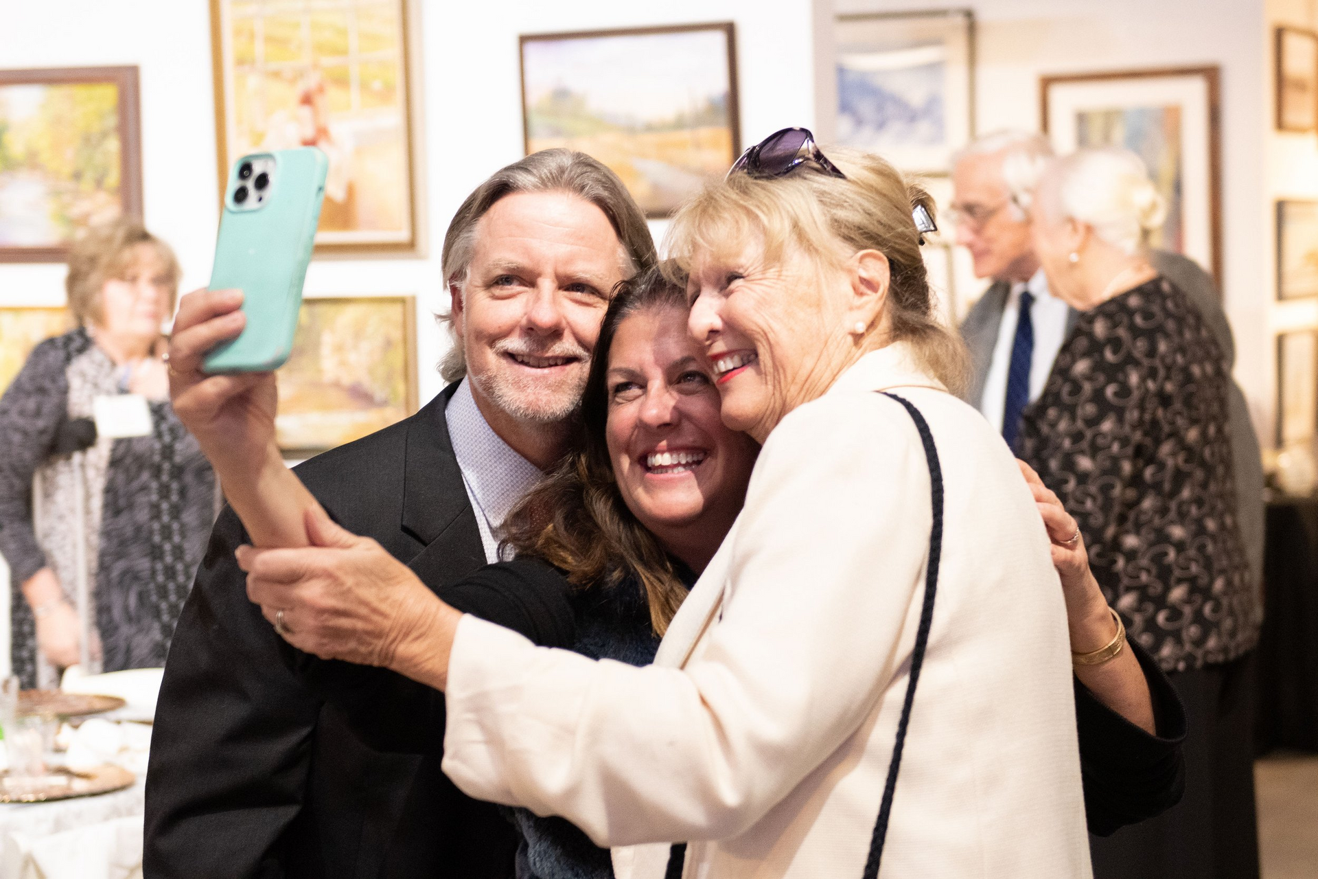 A man is taking a selfie with two women in an art gallery.