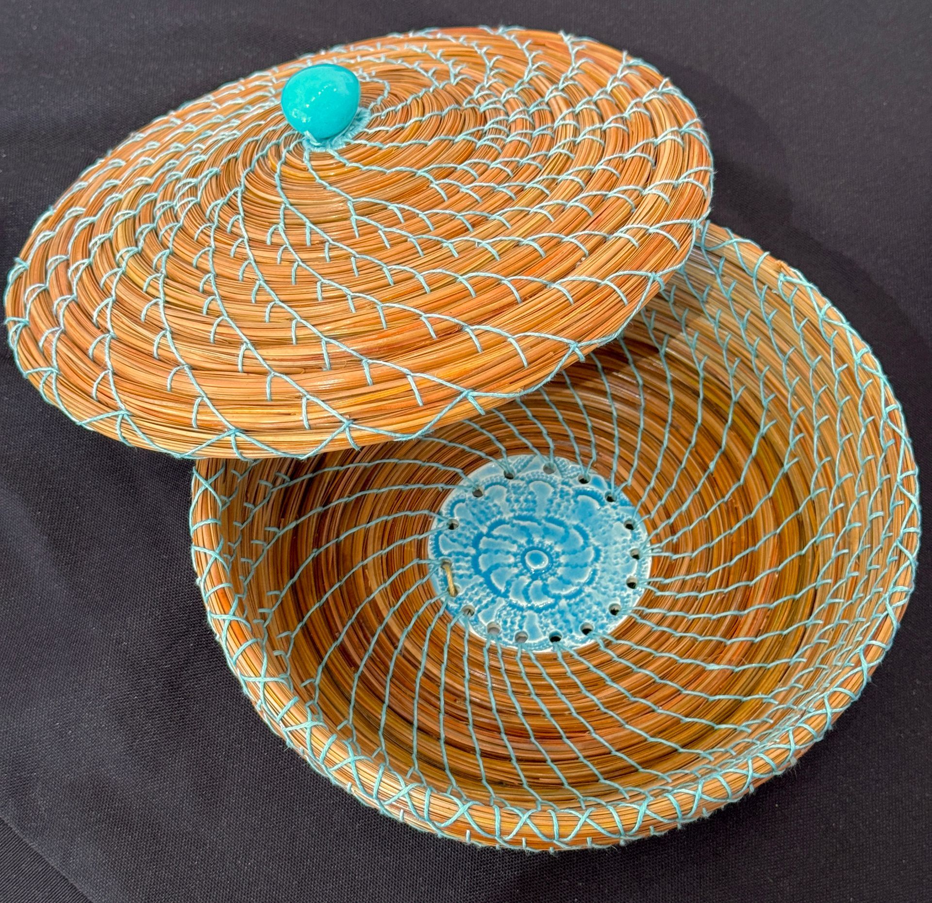 Two woven basket lids, orange and tan with blue accents, stacked on dark fabric background
