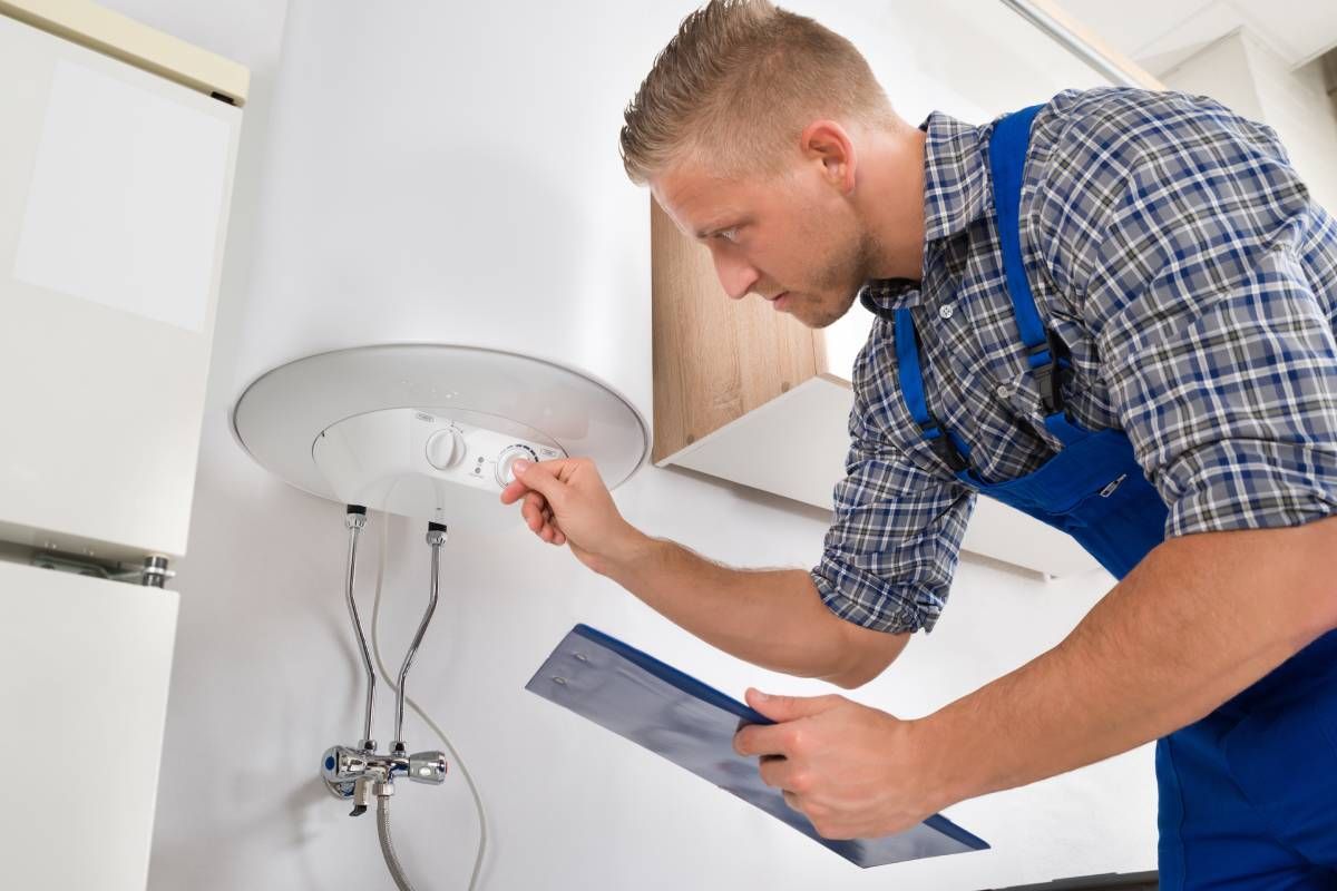 Worker in blue plaid and blue overalls adjusting a water heater's temperature near Somerset, Kentuck