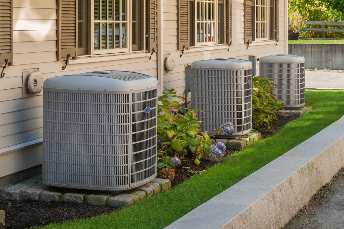 Three residential HVAC units outside condo windows in a well-manicured landscape and blue flowers near Somerset, KY