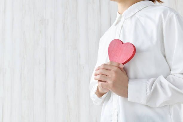 A woman in a white shirt is holding a red heart in her hands.