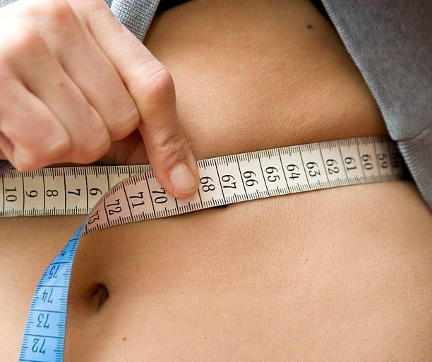 A person is measuring their stomach with a tape measure