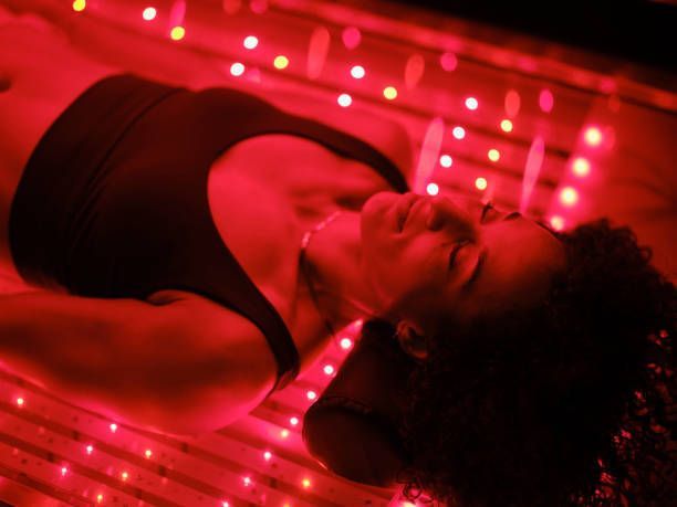 A woman is laying on a bed with red lights on her body.