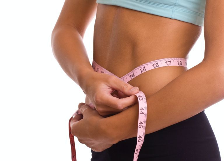 A woman is measuring her waist with a tape measure