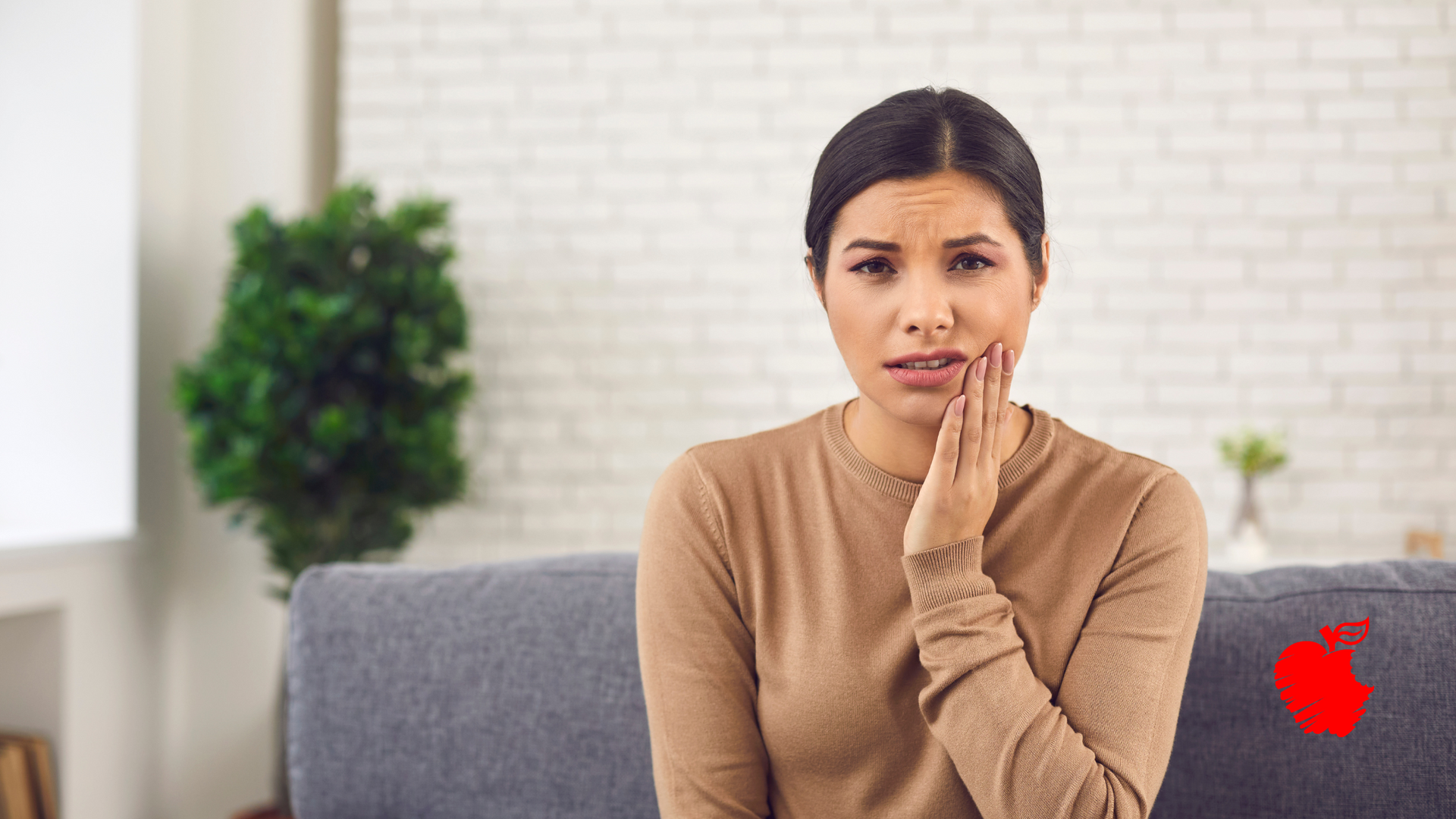 A woman is sitting on a couch with a toothache.