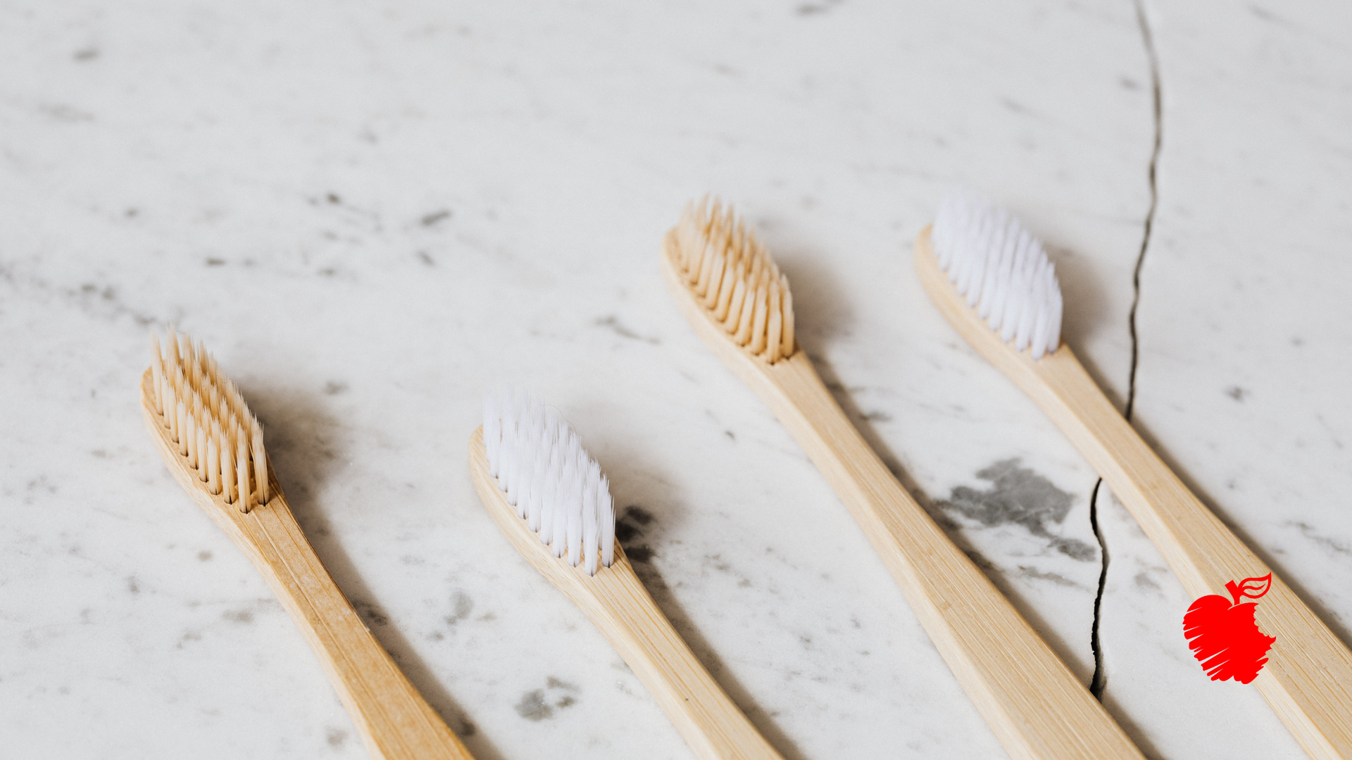 Four bamboo toothbrushes are lined up on a marble counter top.