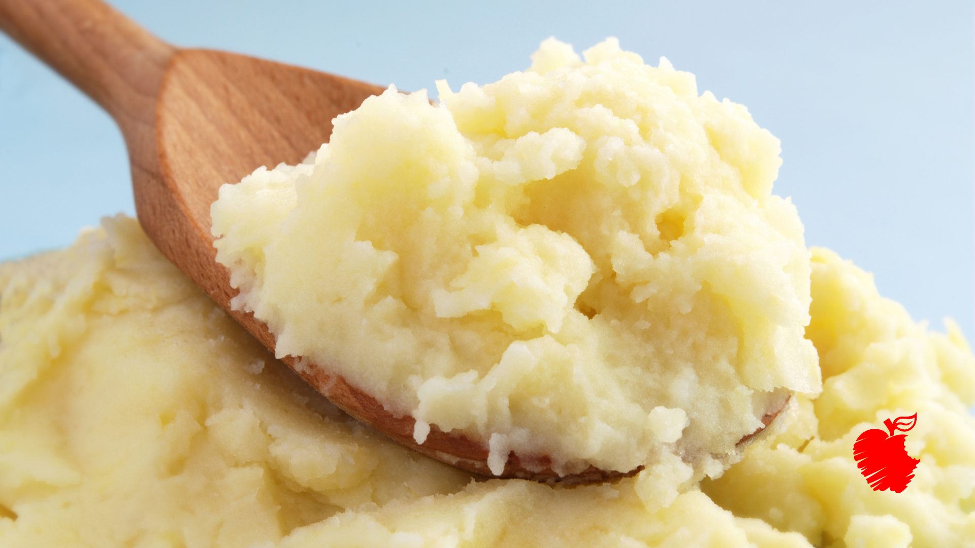 A wooden spoon filled with mashed potatoes is sitting on top of a pile of mashed potatoes.