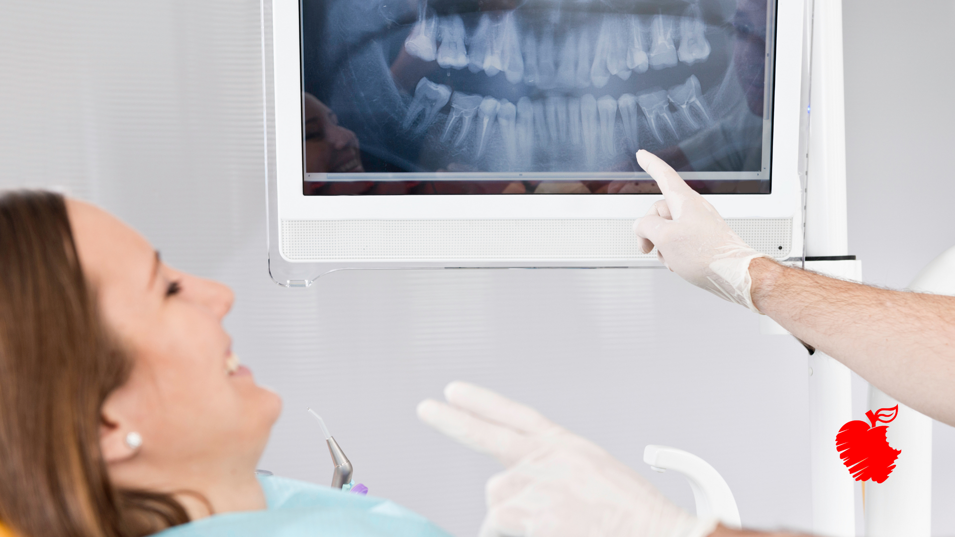 A woman is sitting in a dental chair looking at an x-ray of her teeth.