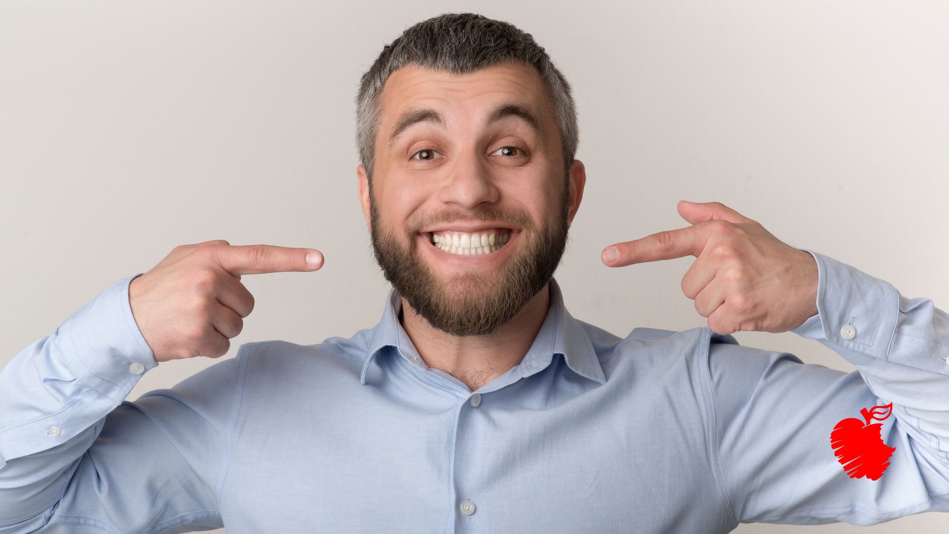 A man with a beard is pointing at his teeth and smiling.