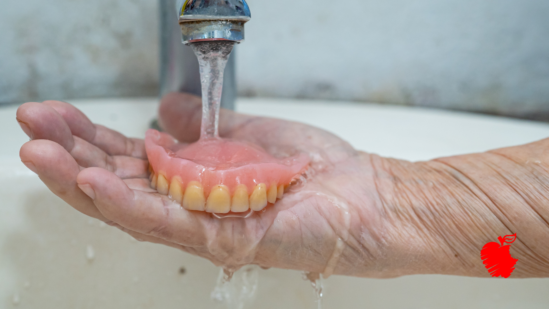 A person is washing a denture in a sink.