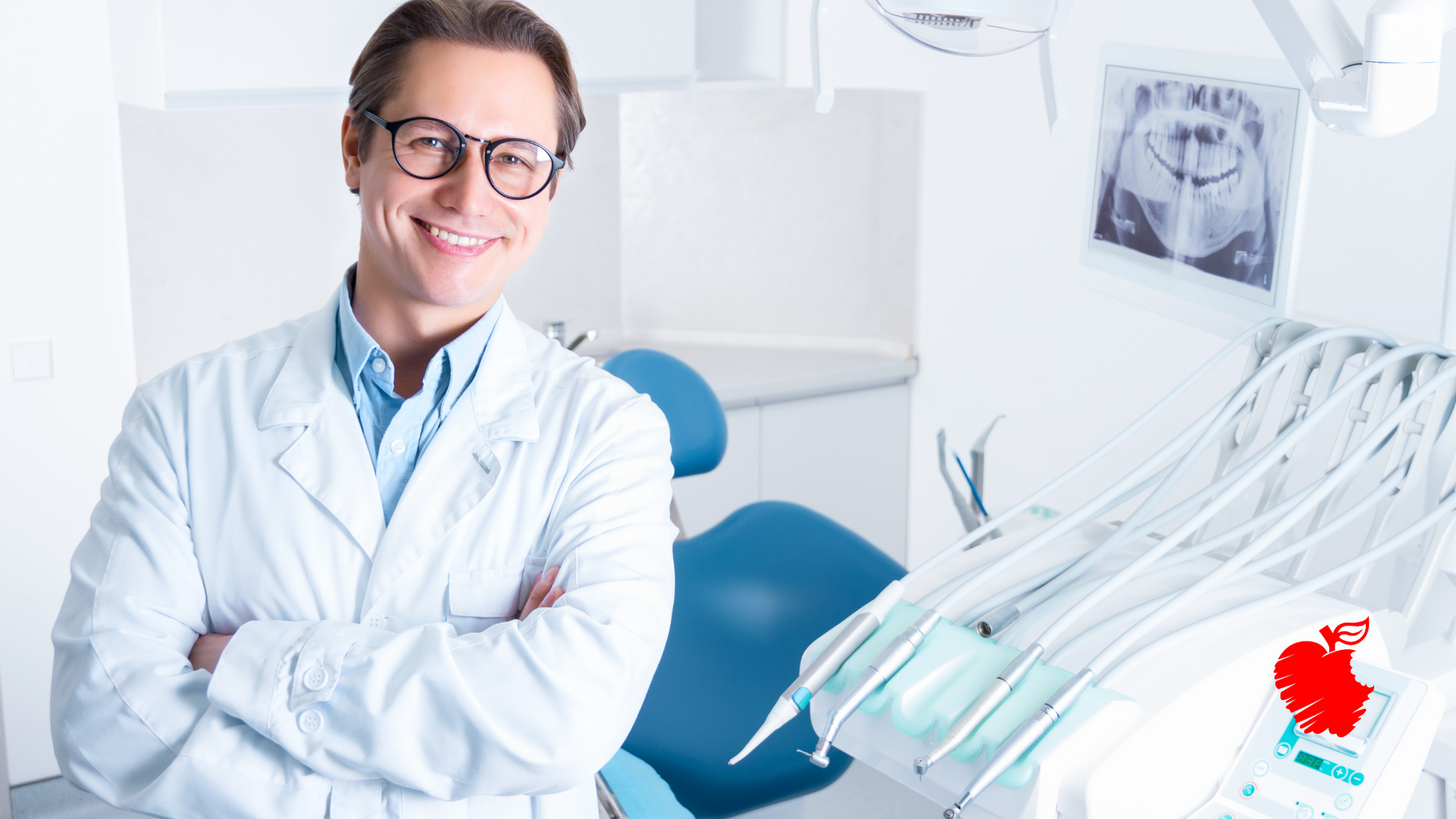 A dentist is smiling in a dental office with his arms crossed.