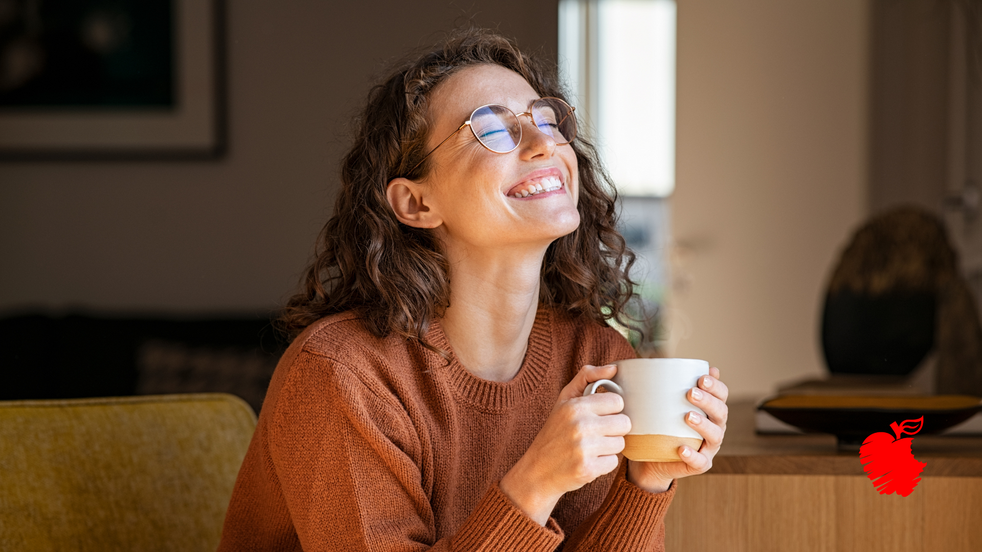 A woman is sitting on a couch holding a cup of coffee and smiling.