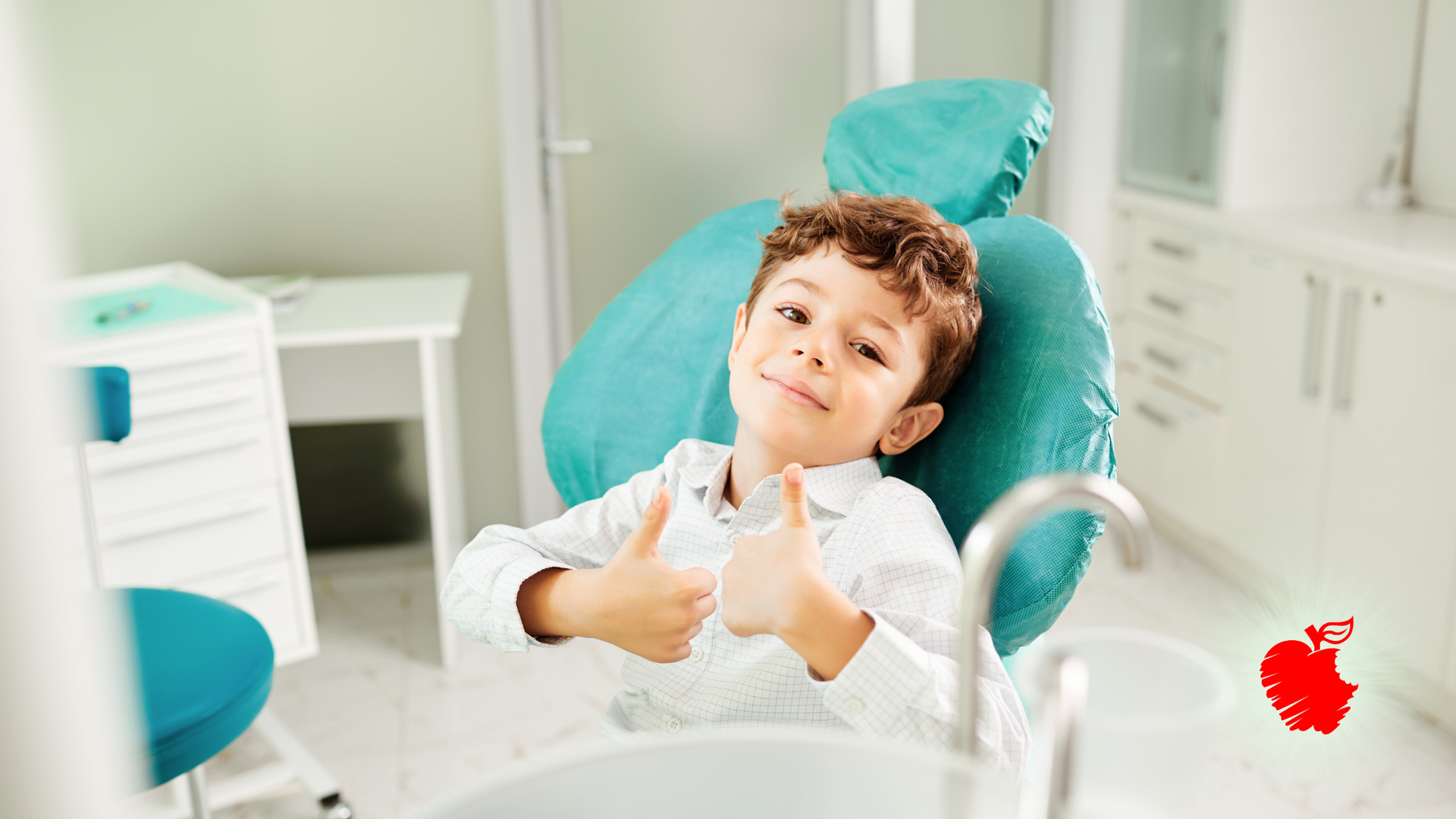 Boy in a dental chair gives a thumbs up. He's in a white dental room with a teal chair.