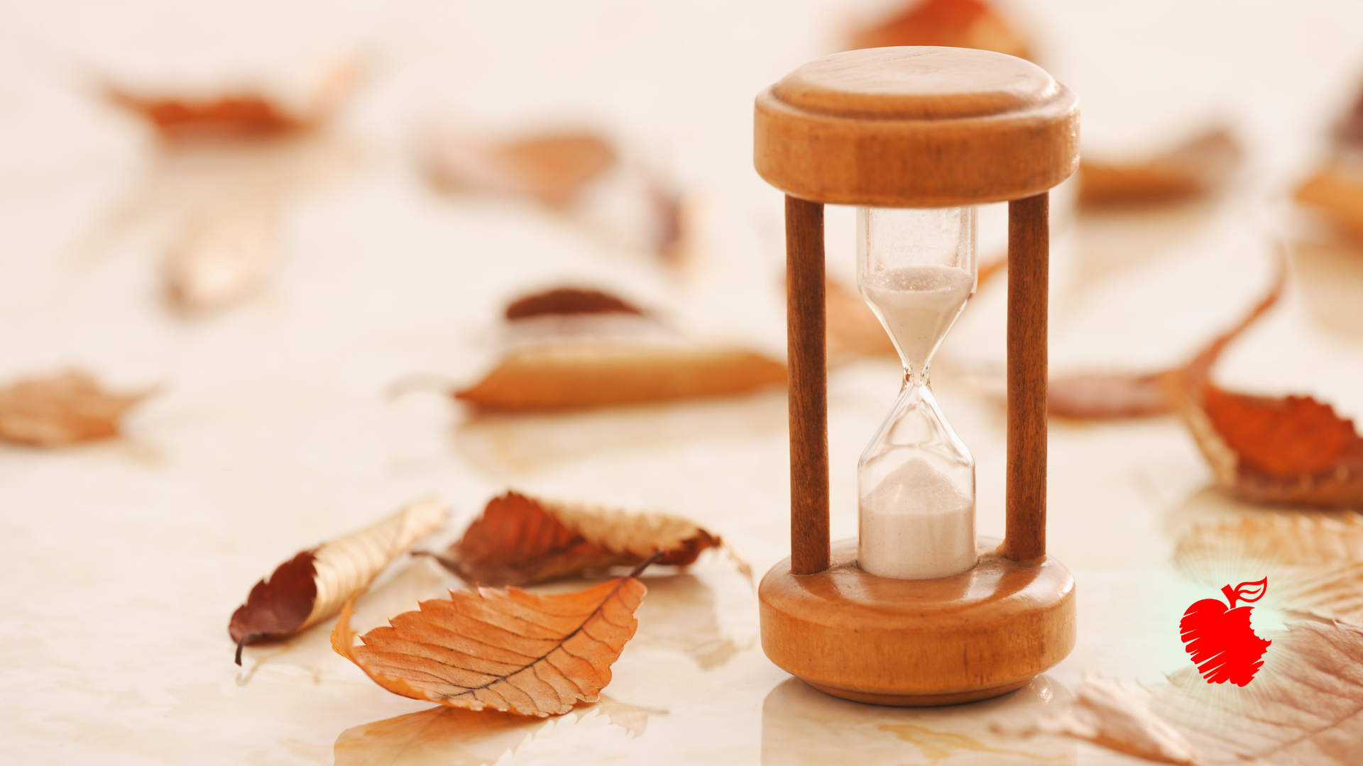 Hourglass with sand falling, surrounded by autumn leaves.