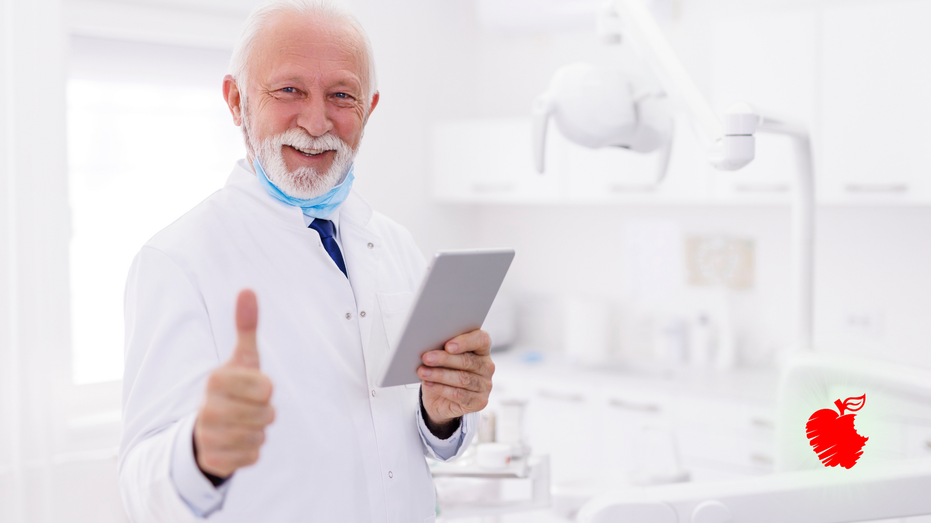 Smiling, elderly dentist holding tablet, giving thumbs up in dental office.