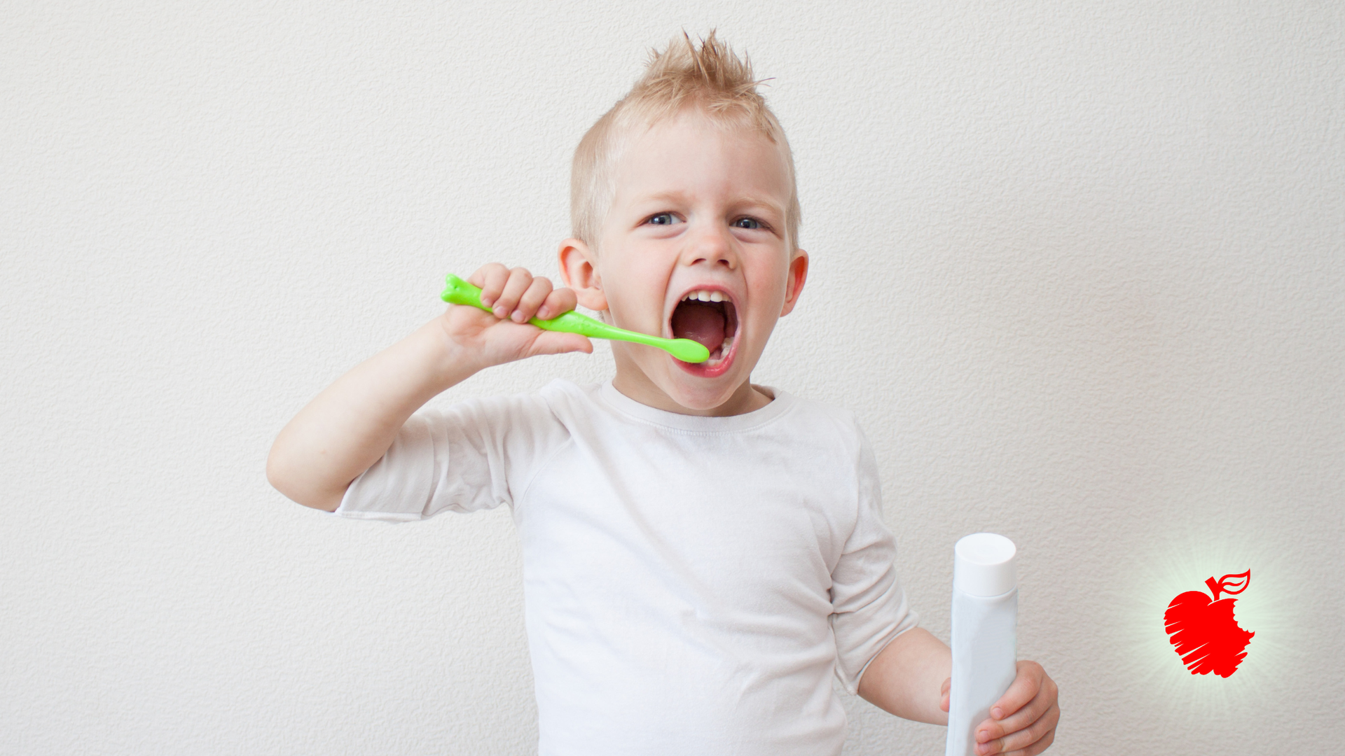 Young child brushes teeth, holding toothbrush and toothpaste, open mouth.