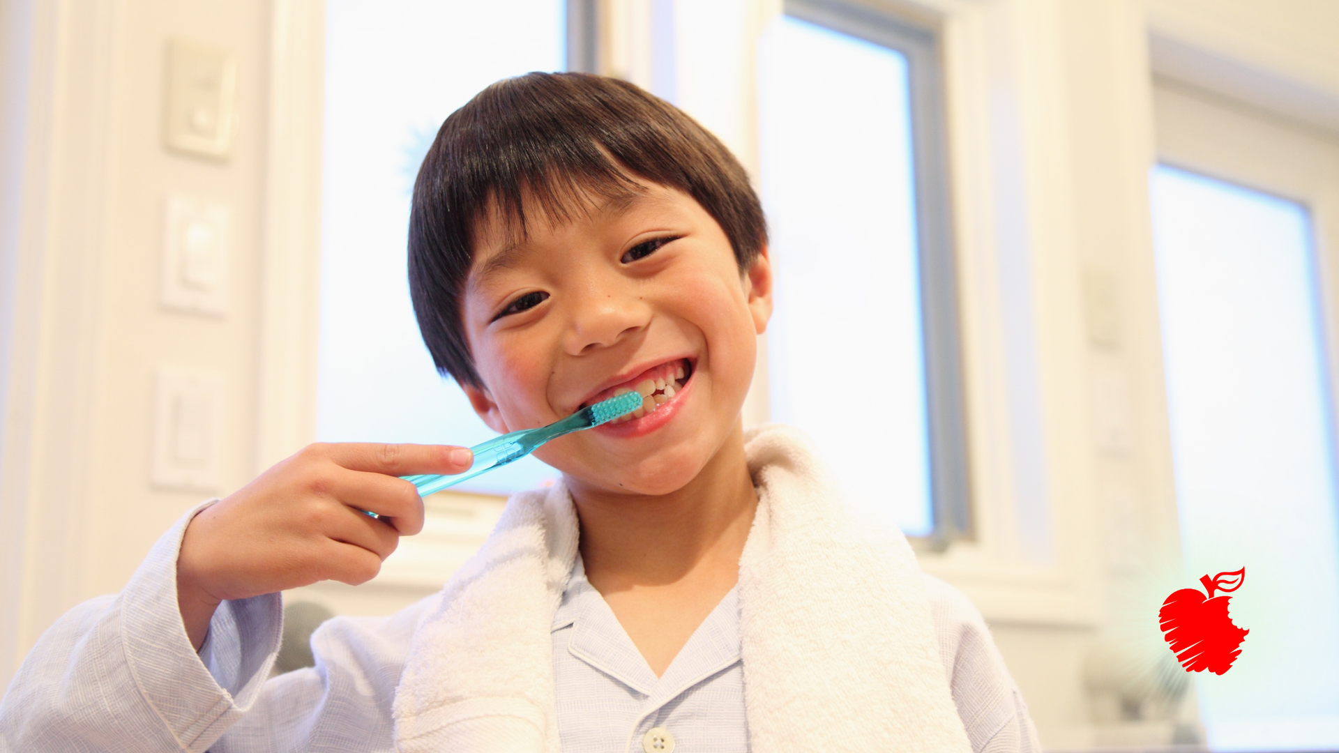 Boy brushes his teeth, smiling in a well-lit bathroom, with a white robe and a clear blue toothbrush.