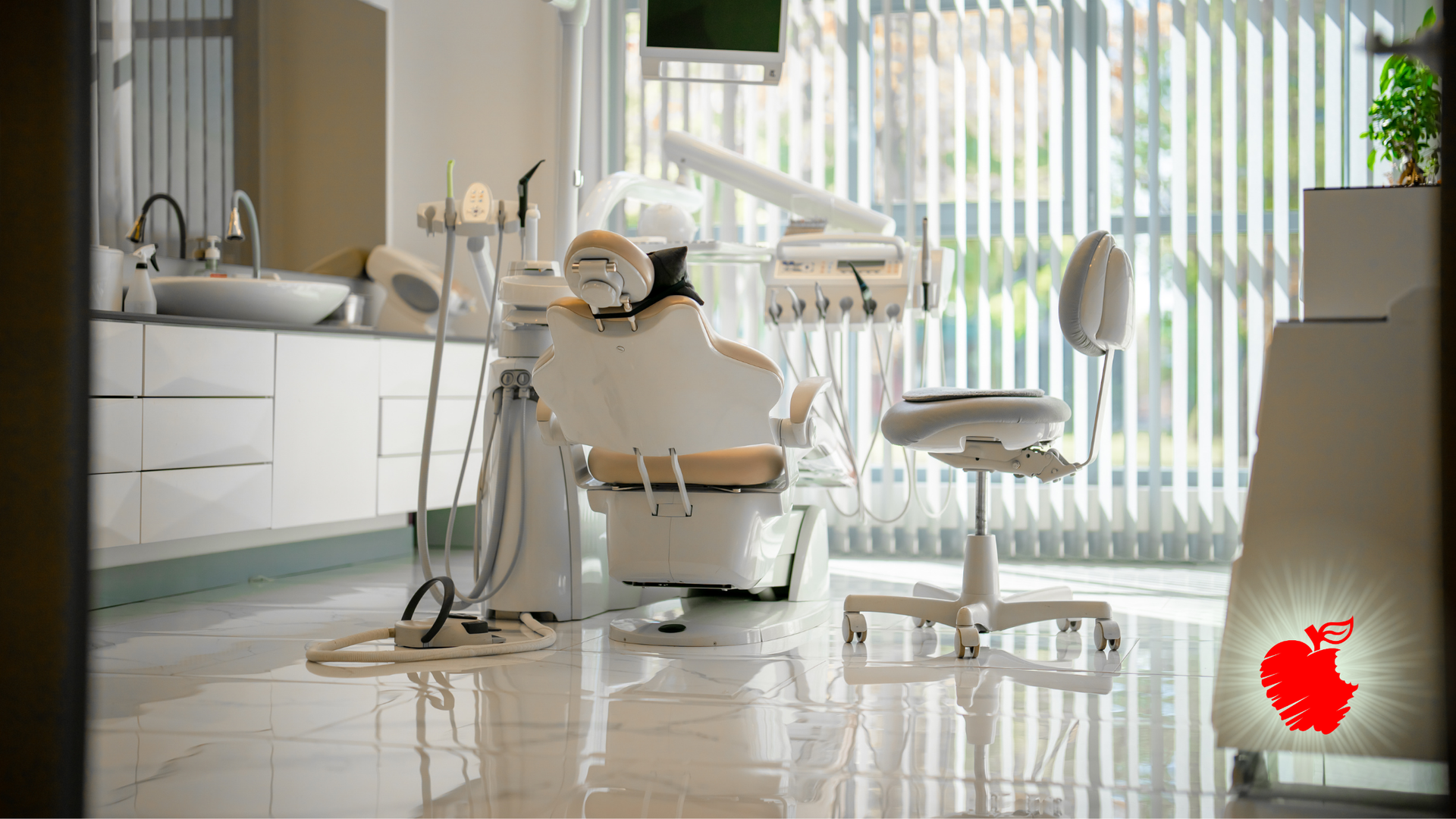 Dental office interior: white chair, equipment, sink, window with blinds, shiny floor, and a red apple logo.