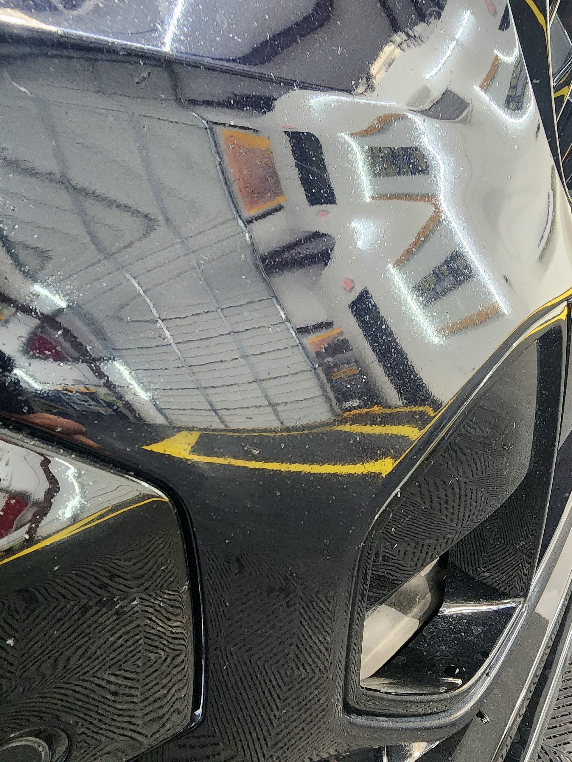 Close-up of a black car bumper reflecting a building with yellow parking lines.