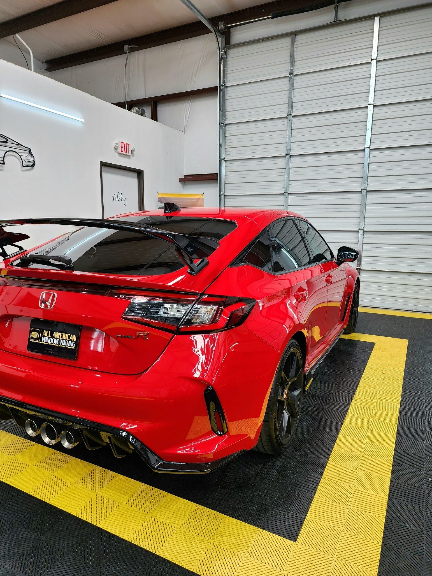 Red Honda Civic Type R in a garage, next to a closed roll-up door.