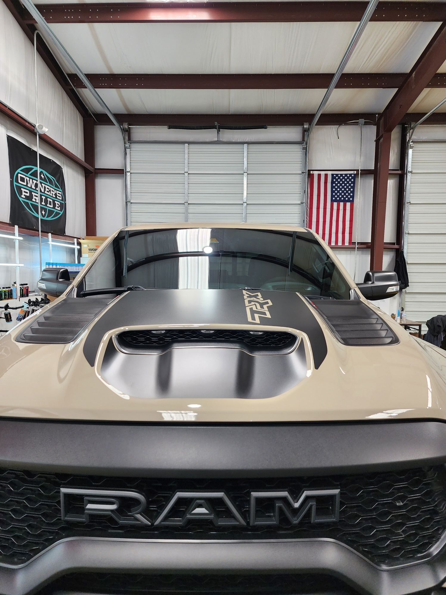 Tan RAM TRX truck inside a garage with an American flag, and a garage door in the background.