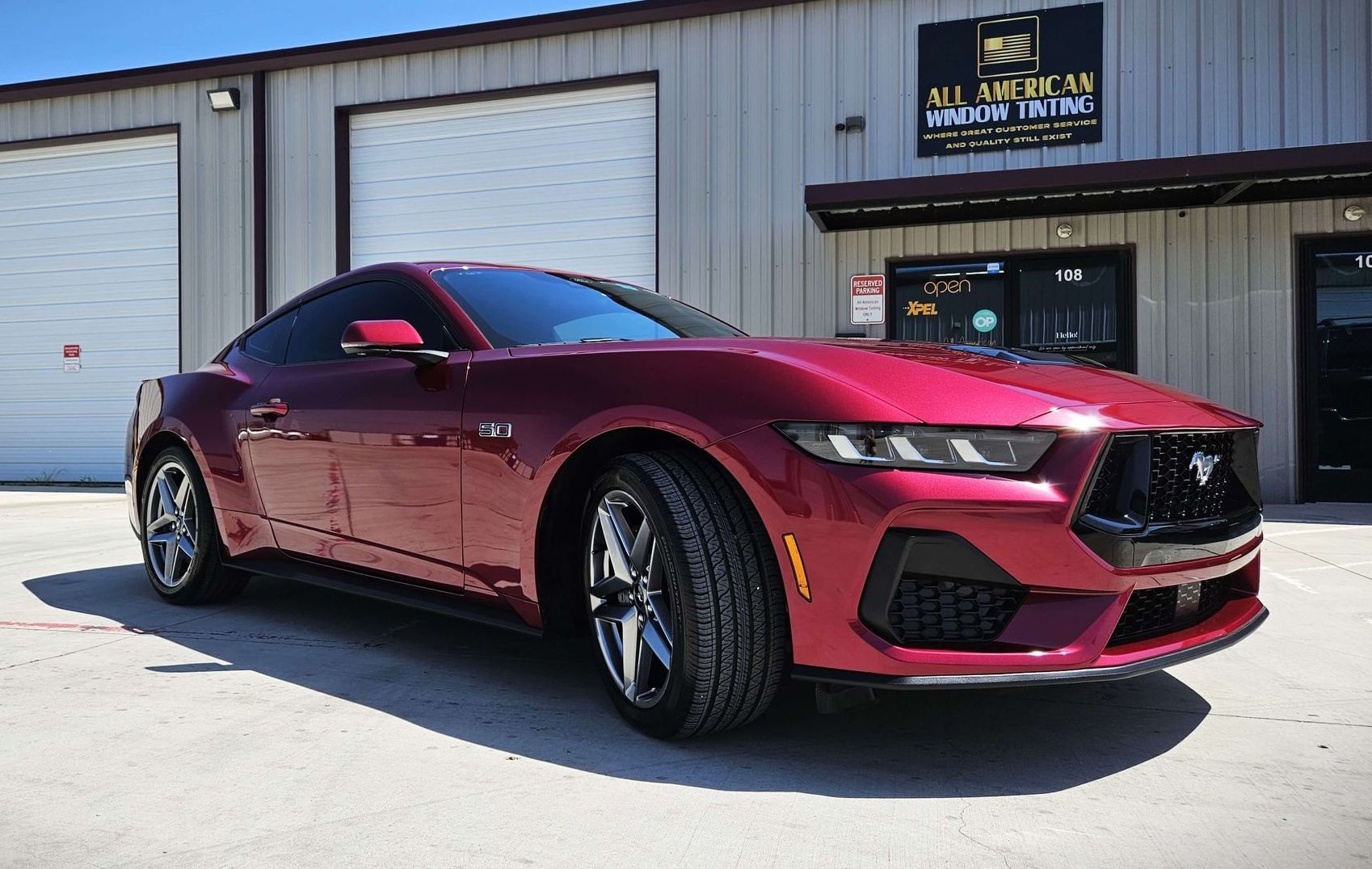 A red mustang is parked in front of a building.