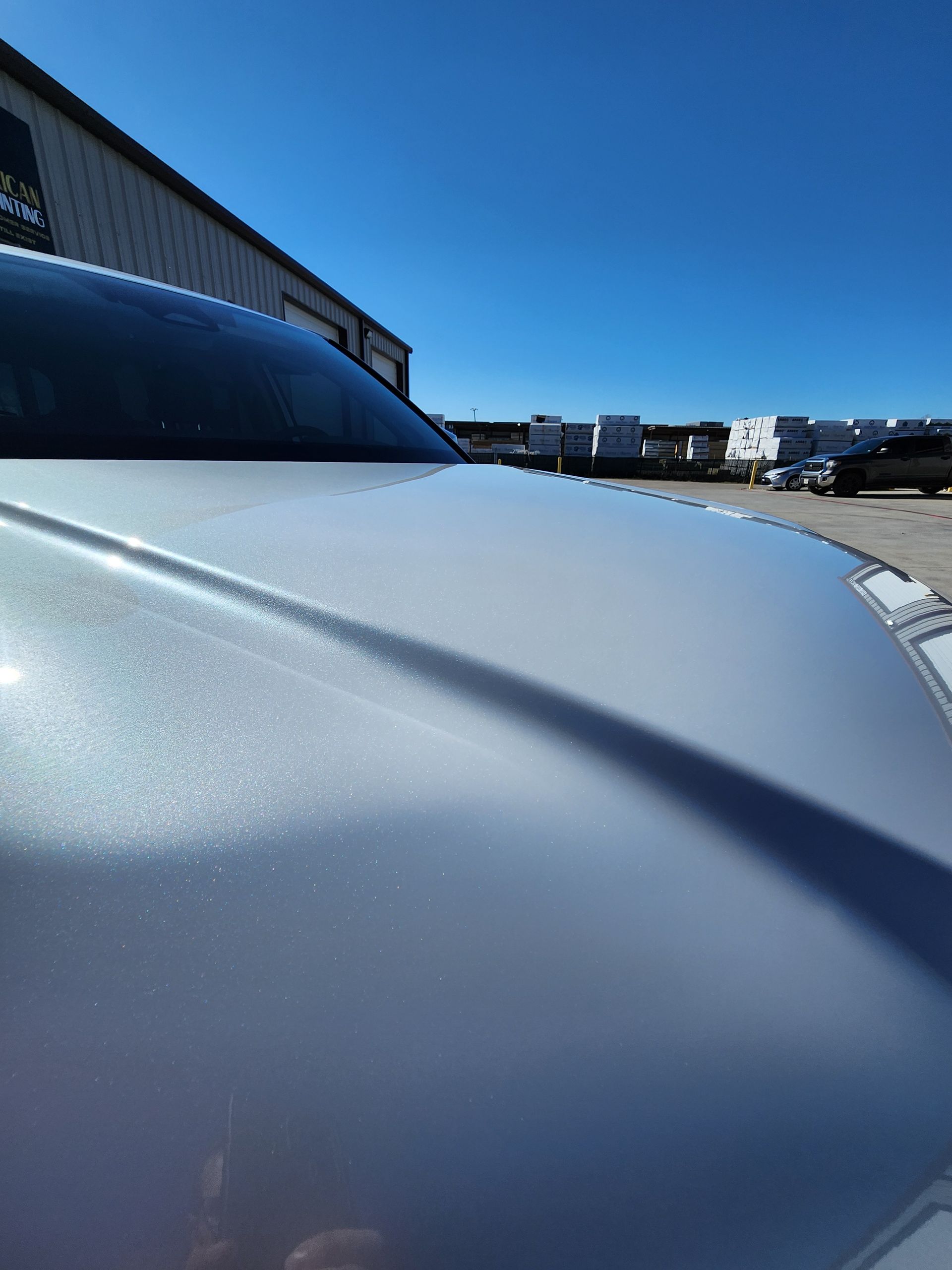 Silver car hood reflecting the bright blue sky with a glimpse of a building in the background.