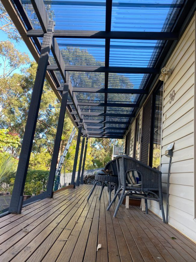 A Wooden Deck With Chairs And A Table Under A Clear Roof — Newcastle Patio Covers In Wallsend, NSW