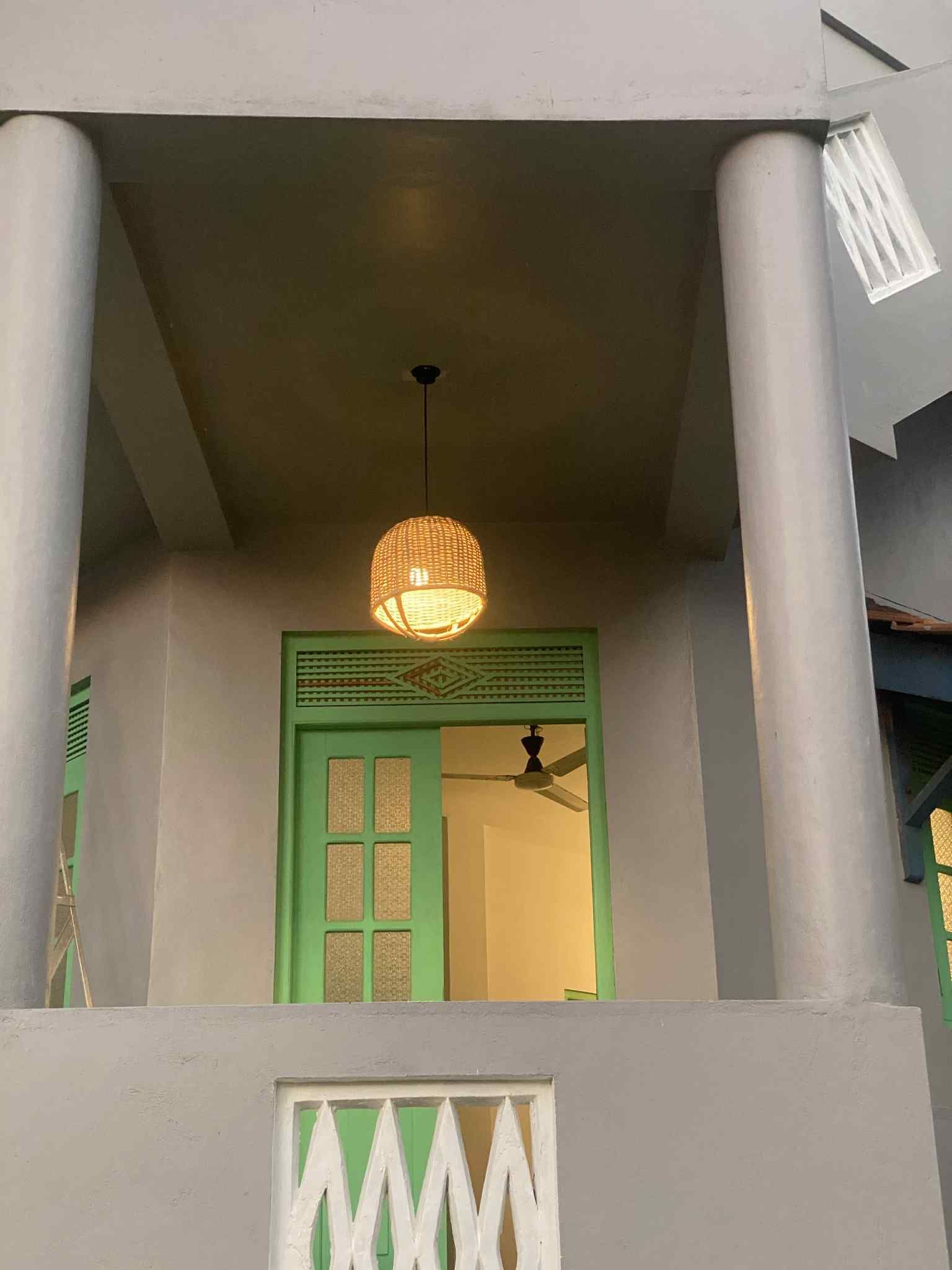 Gray balcony with green door, hanging woven light, and two support columns.